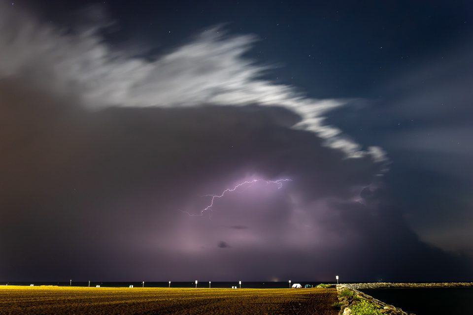 Gewitter beim Abzug, mit direkt klarem Sternenhimmel dahinter. Der helle Saum der Wolken kommt vom Mond über dem Gewitter.